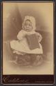 [Baby wearing bonnet and glasses holding a book]