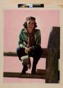 [Woman in cowgirl clothing sitting on wooden fence]