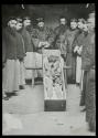 [Group of men posing with dead body in coffin]