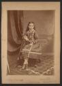 [Seated girl with bows on dress and legs crossed]