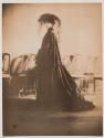 [Olga De Meyer, standing in late 19th Century costume with hat and veil]