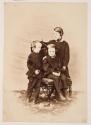 [Two boys and a young girl by a carved chair]