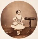[Young girl standing by table with daguerreotype]
