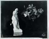 [Small statue of a nude woman next to flowers]