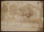 [Street view with three and one-half story brick structure, iron fence]