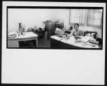 [Two women (topless) seated at desks]