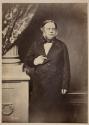 [Middle aged man, standing by column (3/4 length portrait)]