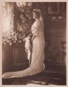 [Bride holding bouquet with flowers in background]