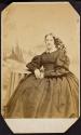 [Woman in dark dress, seated in front of painted backdrop]