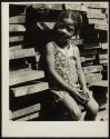 [Girl holding a tennis ball while sitting in front of a pile of wood planks]