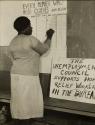 [Woman signing wall chart for Unemployment Council members needing clothing]
