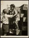 [Little boy helping little girl down from stack of wood]