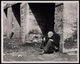 [Homeless man seated under bridge with graffiti “East River Boys"]