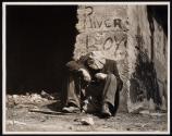 [Homeless man seated under bridge with graffiti “East River Boys"]