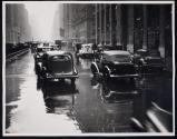 [Automobiles on wet city boulevard]