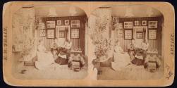 [Three women in a sitting room, one with a photographic album and two sewing]