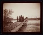 [Group standing on train tracks over the water, woman carrying Kodak #4 case on neck]