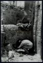 [Interior of bombed building, man crouching in rubble]
