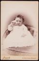 [Baby, seated on upholtered chair with shell to ear]