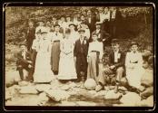[Group of 28 young men and women, standing and sitting on rocks by riverbed]