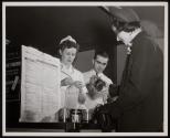 Preparation for Point Rationing: With Official Table of Point Values for Processed Foods prominently posted, a shopper awaits wrapping of her purchases while clerk removes point stamps from War Ration Book Two.
