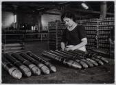 [Woman working on ammunition cylinders in factory]