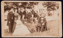 [Group portrait of 8 women and 5 men, seated on lawn at side of house]