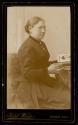 [Woman, seated looking at photo album]