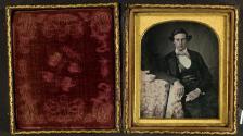 [Young man standing at posing table, small banner at edge of table]