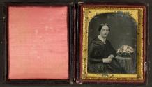 [Woman seated next to posing table with flowers in a basket]