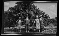 [Family in front of orange tree, woman holds pekingese dog]