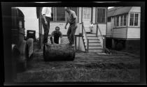 [Three men with lawn roller at cottage]