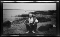 [Dr. Ernst Wilkens seated on rock with two children in his arms]