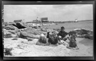 [Four young people, dalmatian dog, on rocky beach]
