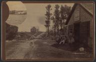 [Man in derby hat, student in striped blazer and beanie and a blacksmith, in front of A.J.H. Turner Blacksmith shop]
