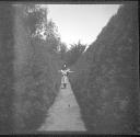 [Woman walking between hedges]