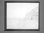 [Man at cliff base and shoreline]