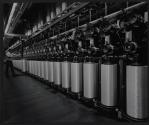 [Worker installing a large spool onto a large machine along with other spools]