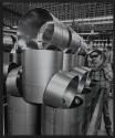 [Worker beside a stack of ductwork looking through a pice of pipe.]
