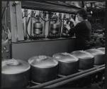 [Worker testing or filling a metal tank.]