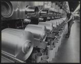 [Worker adjusting a spool of material on a large industrial machine]
