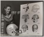 [A model holding up a poster showing the evolution of football helmet design]