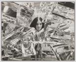 [Woman looking through assembly of shiny metal parts]