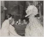 [Two women and two children on the set of Sesame Street with Big Bird.]