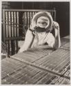 [Technician at electronic component inspection table looking through a magnifier at the camera]
