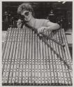 [Worker holding a tubular metal component in a factory setting]