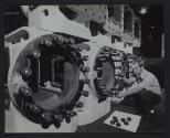 [Technician threading nuts onto large pipe fitting structure]