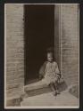 [Girl sitting in doorway of a tenement]