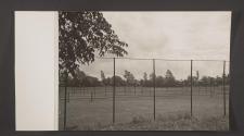 [Column of military trucks on a road behind tennis courts]