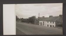 [View of houses along a wide street being used by bicyclists and a woman and child.]